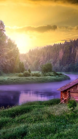 Wooden cabin by a misty river at sunset