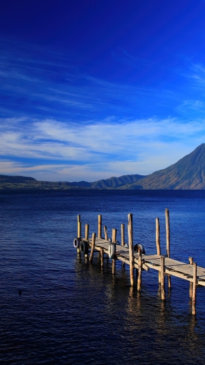 Wooden pier on a deep blue lake with mountains under a bright blue sky