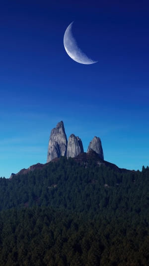 Crescent moon over rocky peaks and forest