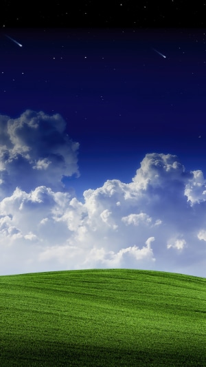 Night sky with shooting stars over rolling green hills