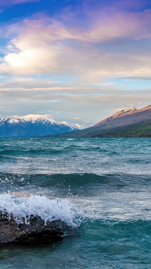 Waves crashing on rocks in a lake with mountains and clouds
