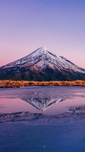 Snow-capped mountain reflected in a frozen lake at sunset