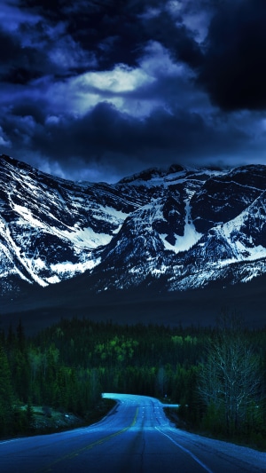 Road leading to snow-capped mountains under stormy clouds