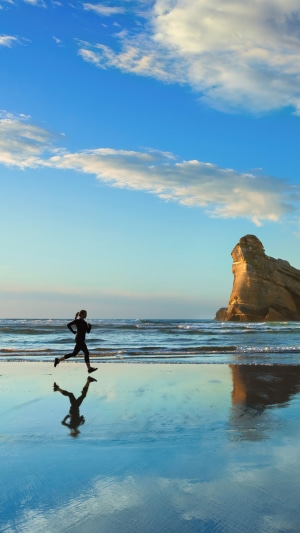 Person jogging on a beach with a rock formation
