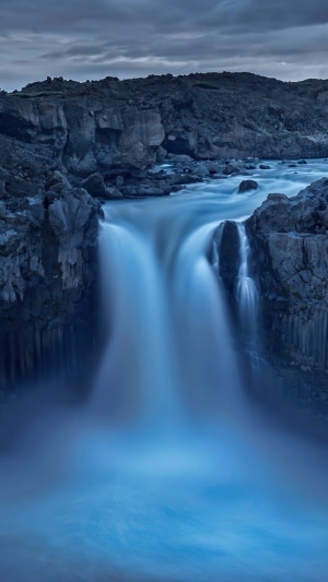 Waterfall flowing over dark rocks under a cloudy sky