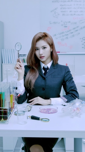 Sana from TWICE holding a magnifying glass in a lab