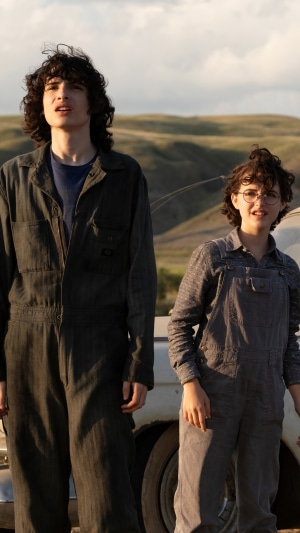 Two children in overalls standing near a car