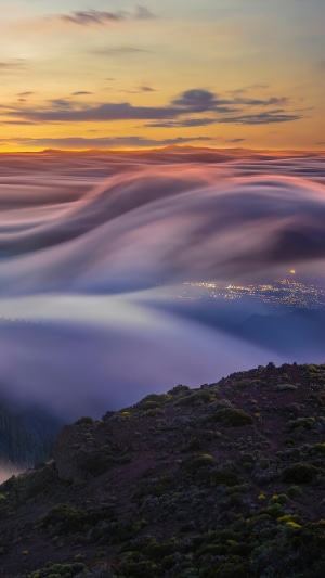 Foggy mountain landscape at sunrise with city lights below