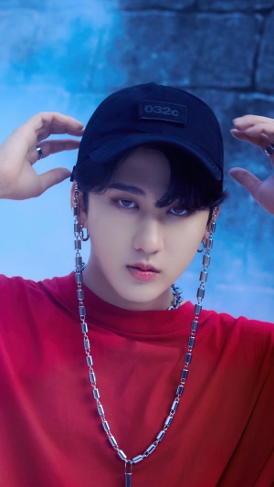 Changbin from Stray Kids wearing a red shirt and black cap