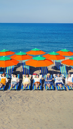 BTS members relaxing on a beach under umbrellas