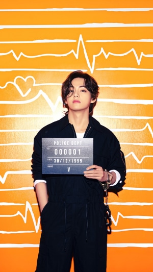 V from BTS holding a mugshot sign