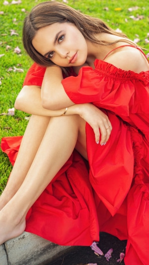 Bailee Madison in red dress sitting on grass