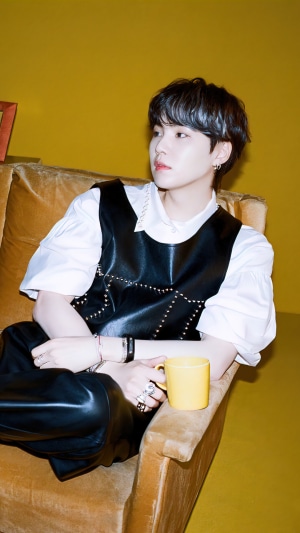 Suga from BTS sitting on a couch with a mug