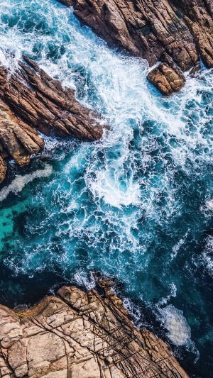 Aerial view of ocean waves crashing on rocky shore