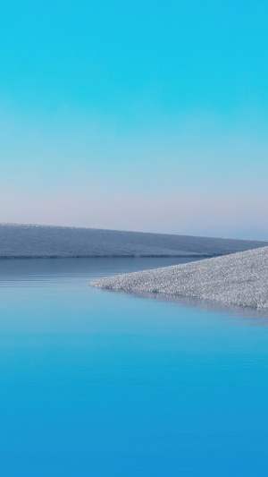 Calm blue water and snow-covered hills under a clear sky