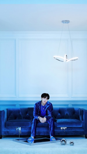 Suga from BTS sitting on a blue couch