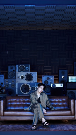 Jungkook from BTS sitting on a couch with speakers