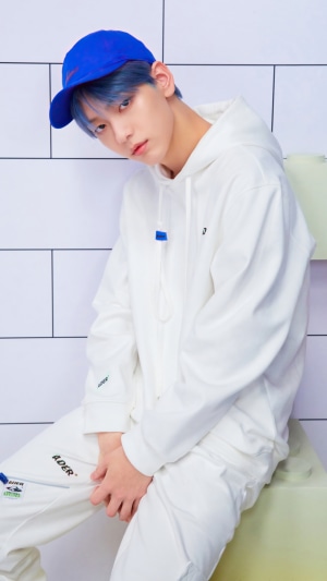 Soobin from TXT wearing a white hoodie and blue cap
