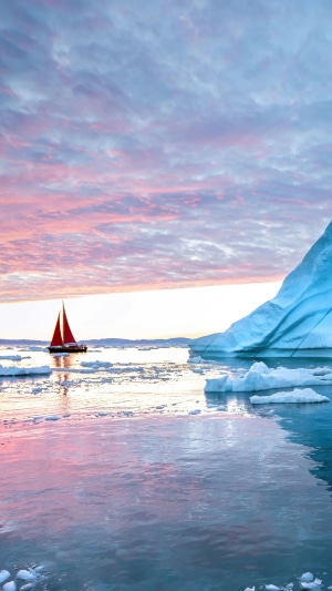 Sailboat near iceberg at sunset