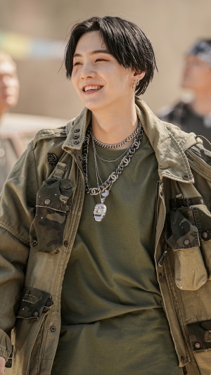 Suga from BTS wearing a green jacket and necklaces