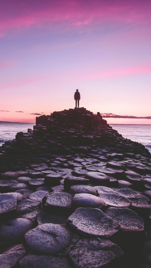 Silhouette of a person on hexagonal rock formations at sunrise