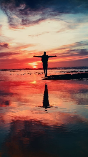 Person with arms outstretched on a beach at sunset