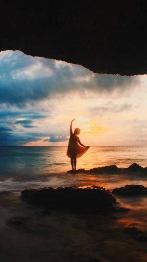 Girl dancing on rocks at sunset near a cave