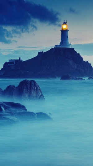 Lighthouse on a rocky island in the sea at dusk