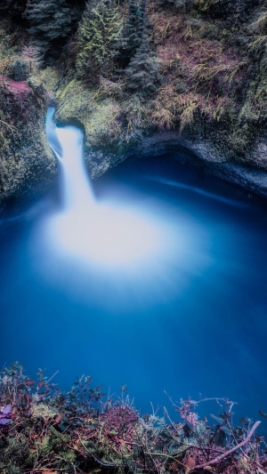 Waterfall cascading into a blue pool surrounded by trees