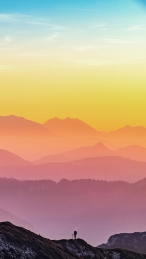 Hiker on mountain ridge with layered mountains at sunset