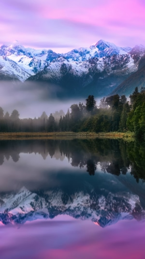 Snow-capped mountains reflected in a misty lake at sunrise