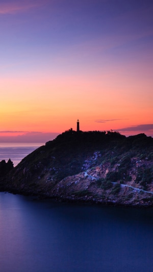 Lighthouse on a hill at sunset over the ocean