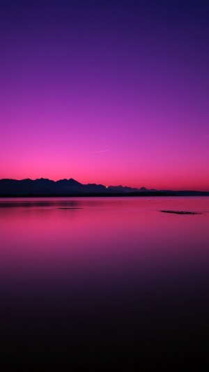 Purple and pink sunset over a calm lake and mountains