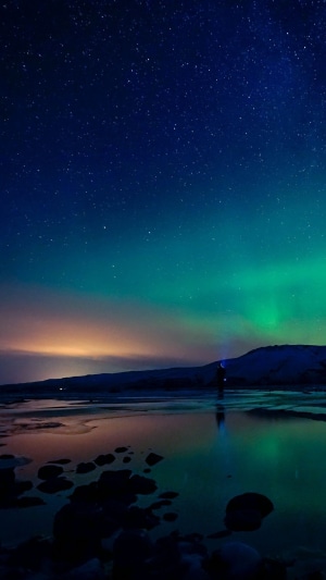 Person watching Aurora Borealis over a reflective landscape