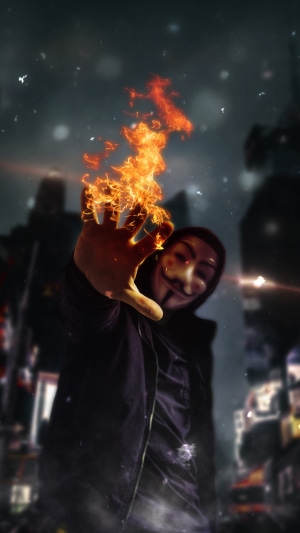 Anonymous hacker with fire on hand in city
