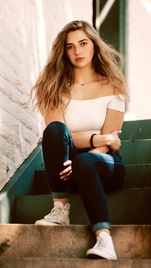 Girl in white off-the-shoulder top and jeans sitting on stairs
