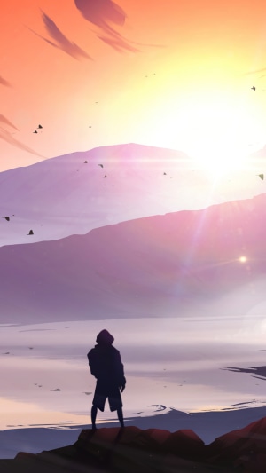 Person standing on rocks watching sunset over mountains