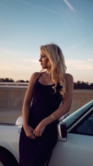 Woman in black dress leaning on a car
