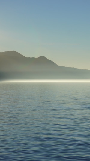 Lake and mountains with fog and airplane contrail