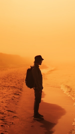 Man with backpack on beach at sunset 4K