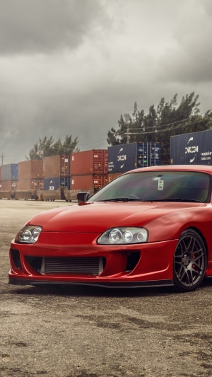 Red Toyota Supra parked near shipping containers