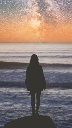 Silhouette of a girl on a rock by the ocean under the Milky Way