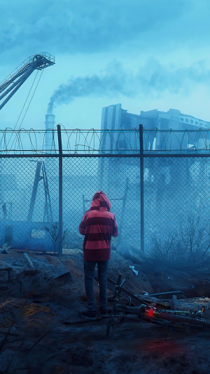 Person in red and striped hoodie looking at factory