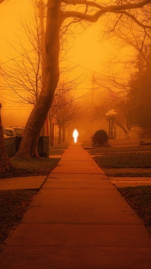 Glowing figure on a sidewalk during an orange haze
