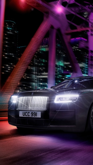Black Rolls Royce Ghost driving on a bridge at night