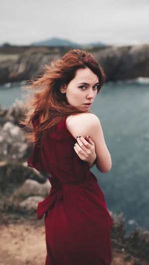 Redhead model in a maroon dress on a rocky coast