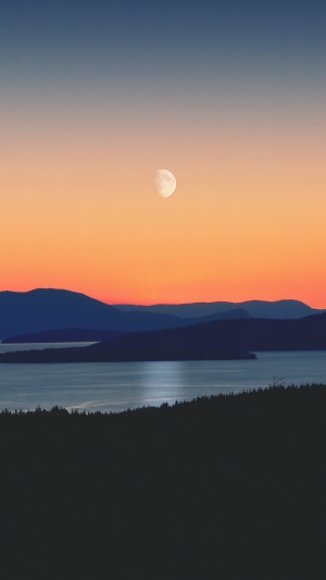 Silhouette of mountains and water at sunset with moon