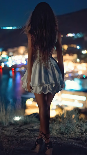 Woman in white dress at night overlooking city lights