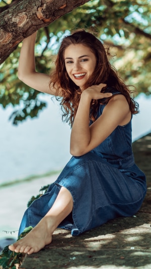 Young woman in denim dress sitting by a tree