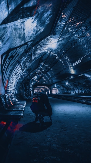 Person in hoodie crouching in a dark subway tunnel